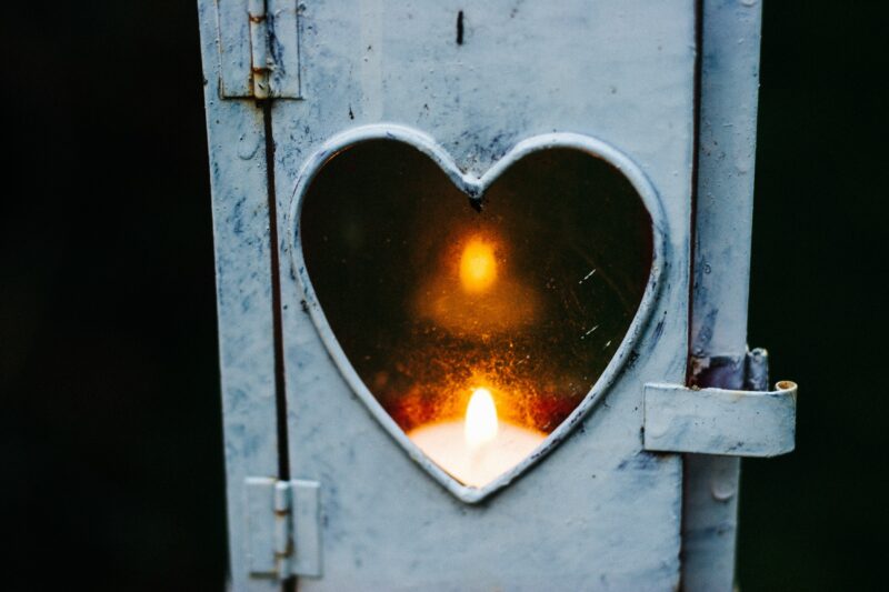 A metal door with a heart-shaped widow. A candle flickers inside the frame of the window.