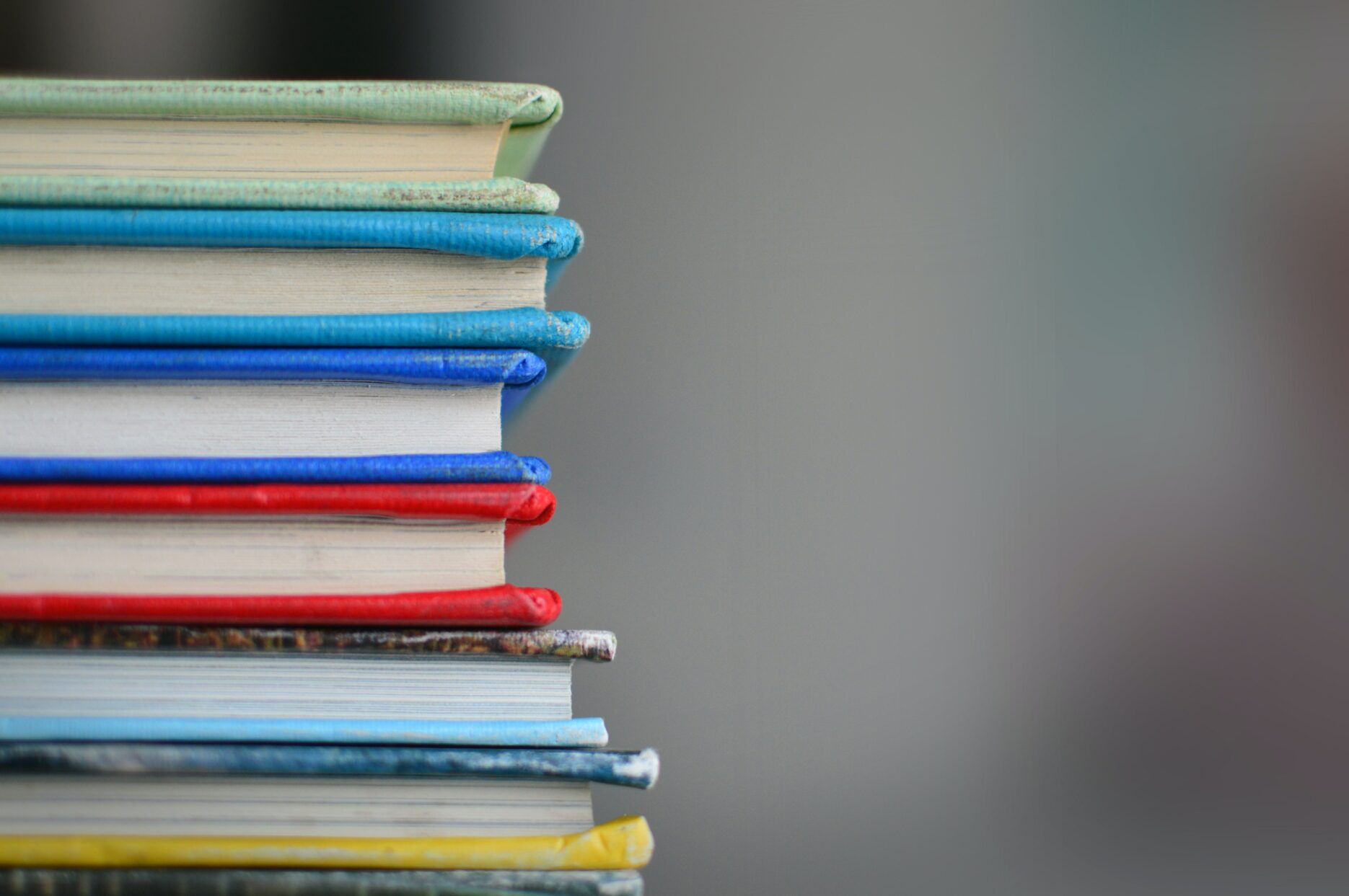 A stack of colourful hardcover books, oriented to the left of the image.