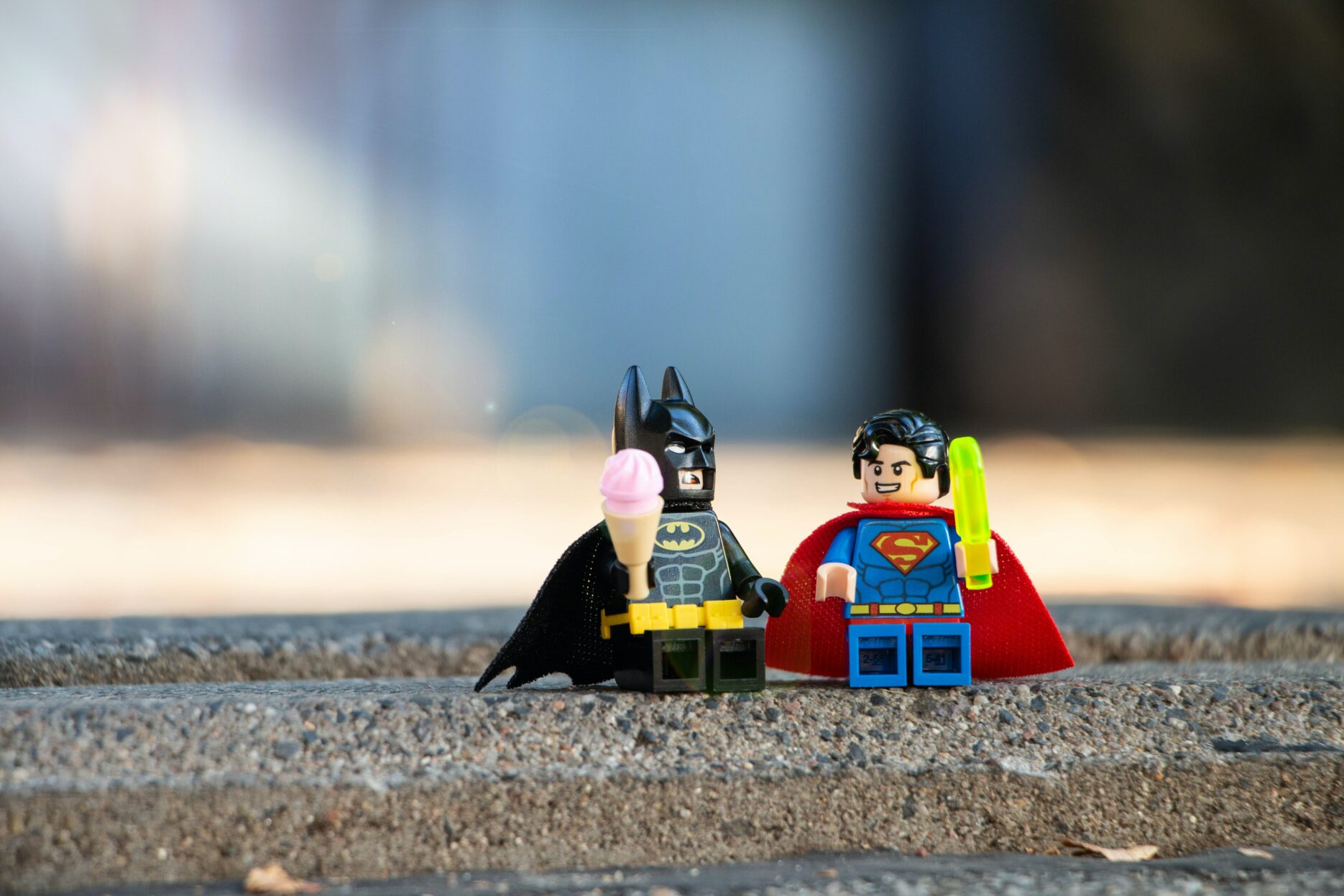 Lego versions of Batman and Superman sit on the pavement eating ice cream.