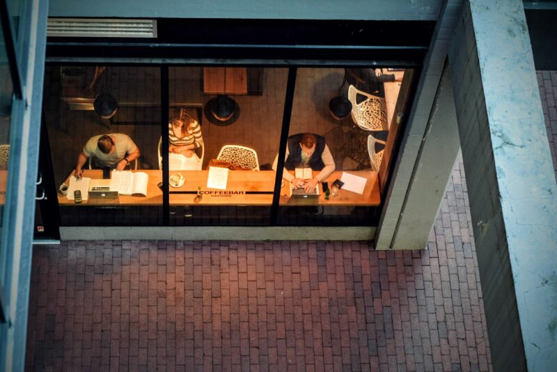 A shot of a coffe shop front window from above. It is night, and people are pictured studying in the front window.