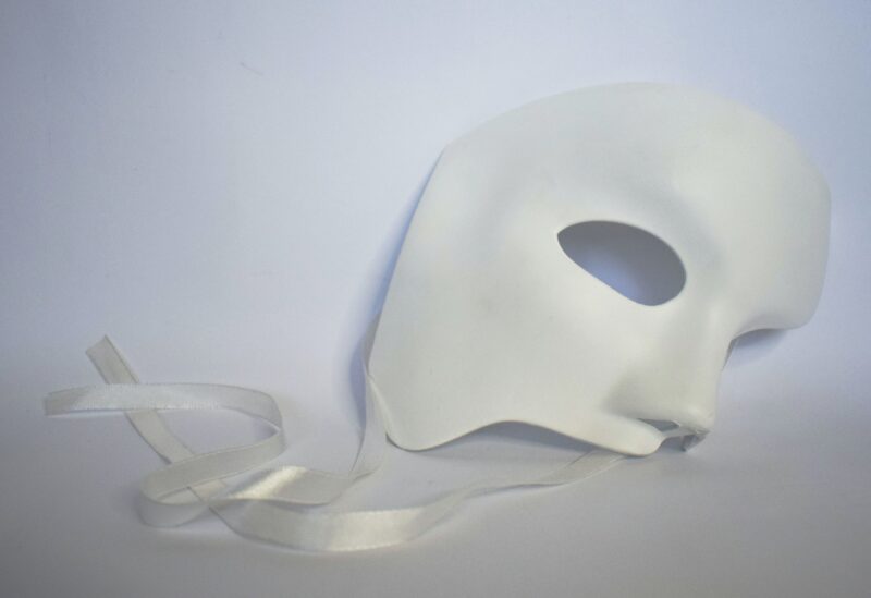 A white drama mask in the style of Phantom of the Opera discarded on a white background.